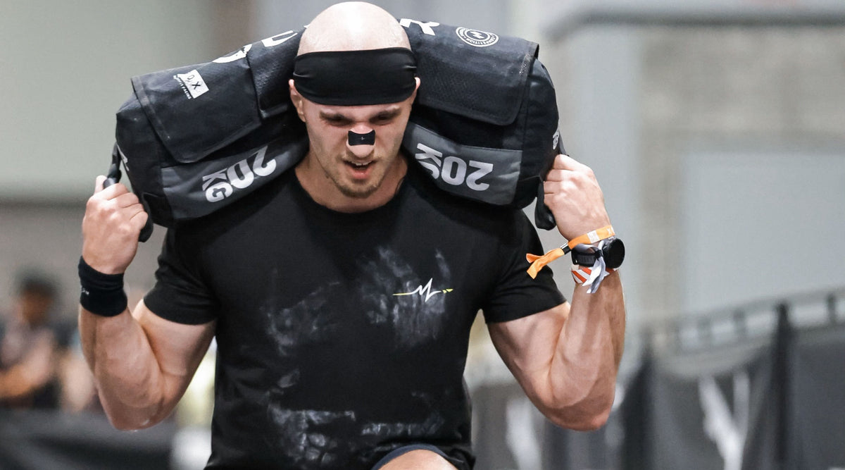 Athlete carrying a 20 kg sandbag at HYROX Washington DC in a KOUXY headband and airflow nasal strip